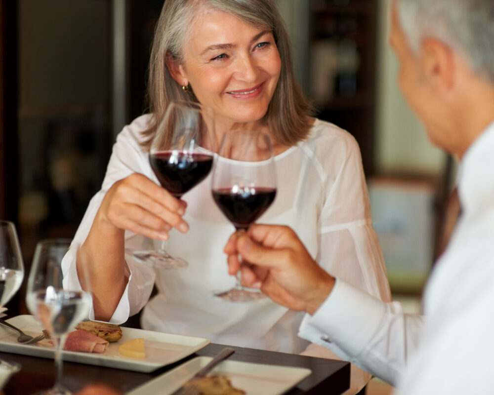 Elderly woman toasting wine with her husband wearing smart clothes for fine dining on cruise - Viking Travel